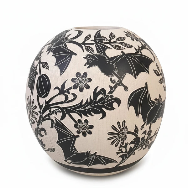 A spherical handmade Mata Ortiz vase with black bats and floral pattern on a cream-colored textured glaze, set against a plain white background.
