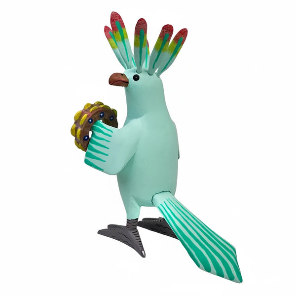 A colorful hand-painted Mexican woodcarving bird figurine holding a green and yellow flower, set against a plain white background.