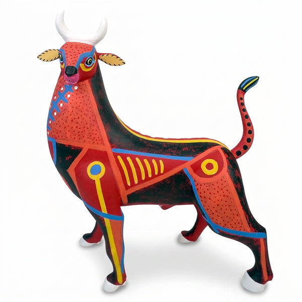 A handcarved , hand-painted Mexican copal wood sculpture of a bull, featuring a vibrant red and black body with geometric patterns in yellow, blue, and white, set against a plain white background.