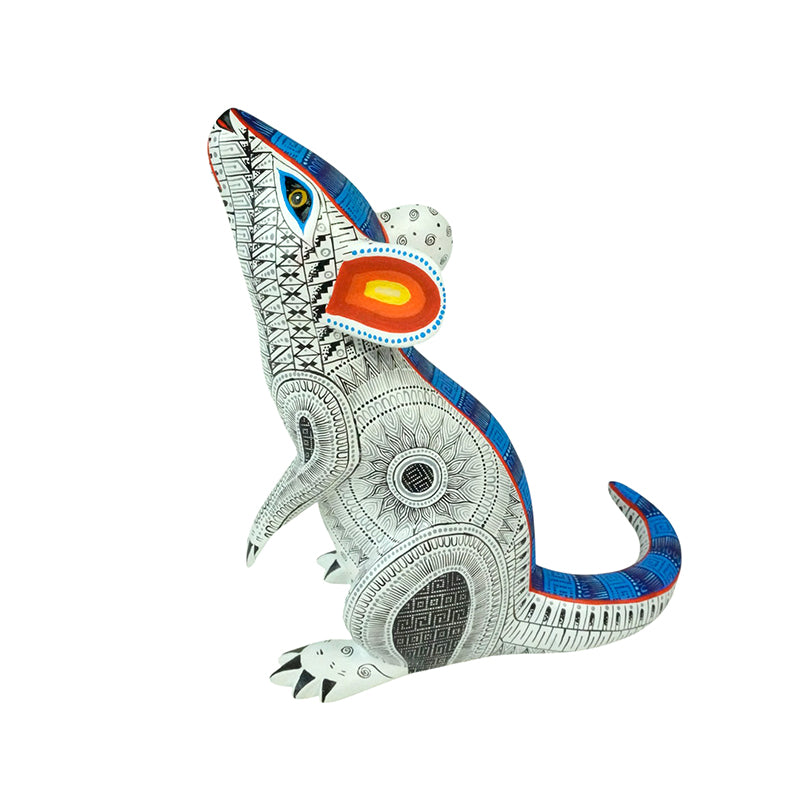 A Oaxacan wood carving of a mouse in white with fretwork designs in blue, red and yellow.