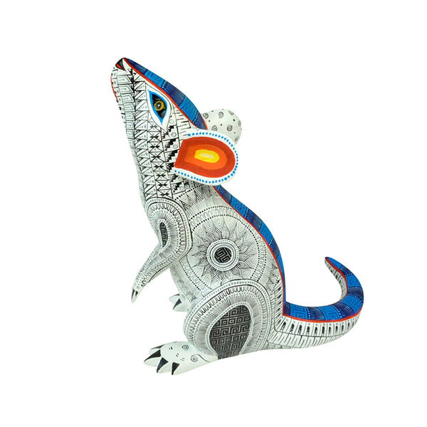A Oaxacan wood carving of a mouse in white with fretwork designs in blue, red and yellow.