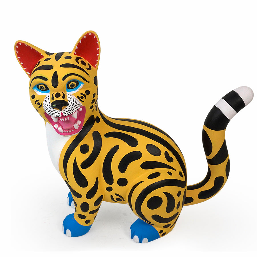 A stylized wild cat copal wood  figurine with a yellow body, black spotted pattern, red inner ears, blue paws, and a black-and-white striped tail, shown on a plain white background.
