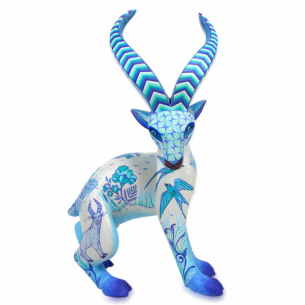 An authentic Oaxacan wood carving  deer figurine with long curved horns, painted in shades of blue, teal, and white with floral and bird motifs, isolated on a white background.