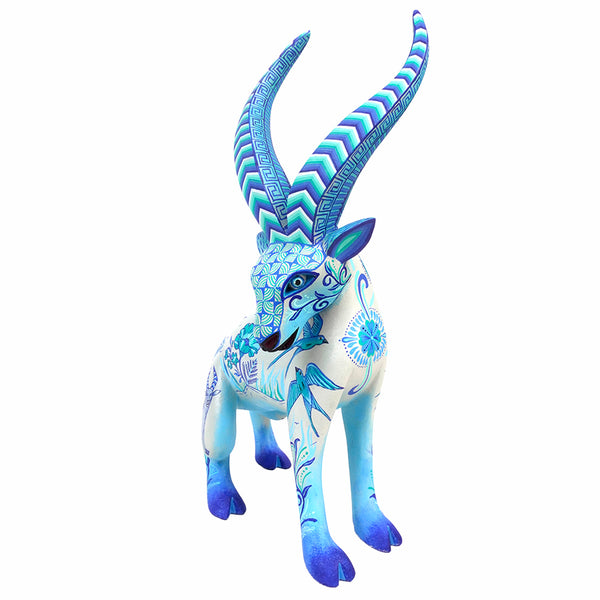Mexican Folk Art wood gazelle figurine decorated with intricate blue and white patterns, featuring long curved horns and a white body with blue floral and geometric designs, set against a plain white background.