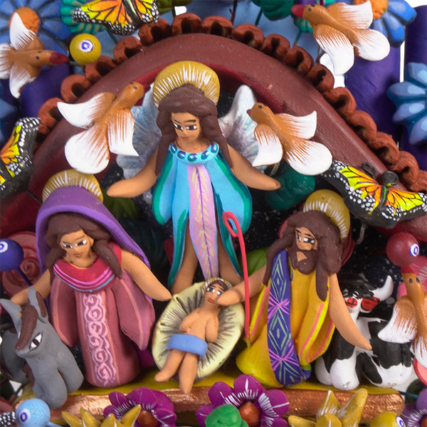 Top portion of a hand-painted clay Tree of Life showing God the Father seated beneath a ring of small flowers, a gold sun and crescent moon on either side, with monarch butterflies and an angel visible just below among purple and blue flowers.