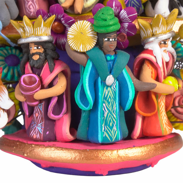 Close-up of the three Wise Men at the base of the Tree of Life, dressed in richly patterned robes and crowns, each bearing a different gift, standing on a gold and pink painted base.