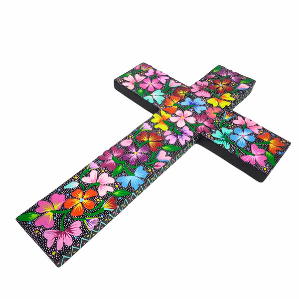 A black wooden cross decorated with a vibrant, colorful Mexican floral pattern featuring pink, orange, blue, yellow, and green flowers on a white background.