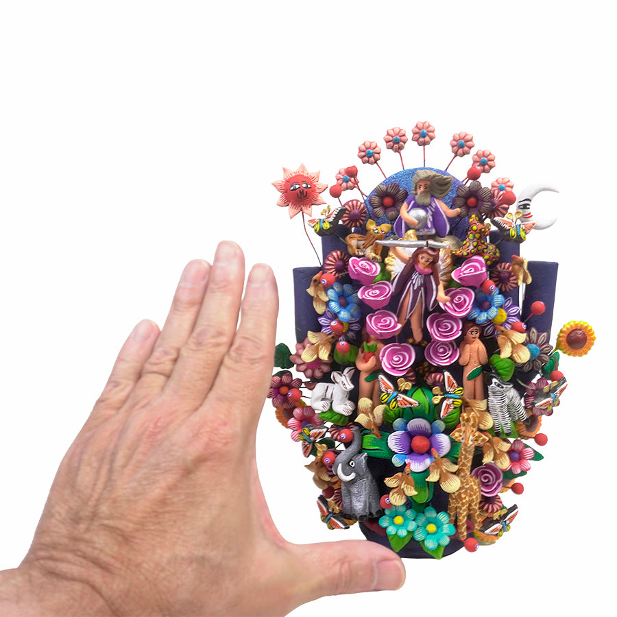 Full view of a hand-painted clay Tree of Life sculpture by the Juan Hernandez family, depicting the Creation story with God at the top holding a globe, a sun and moon on either side, an angel with a sword, Adam and Eve, and Garden of Eden animals throughout.